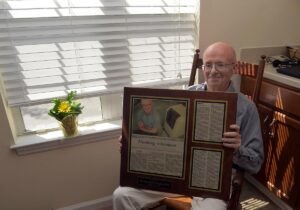 Resident George Keller posing with his plaque with news article