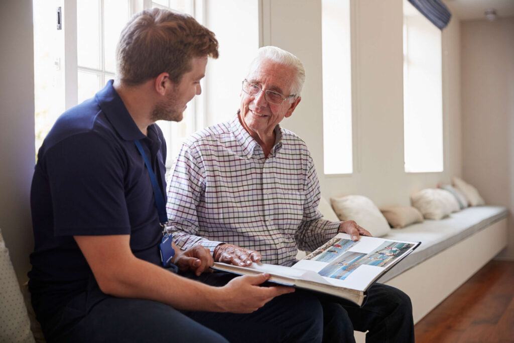 Senior man sitting looking at photo album with male nurse